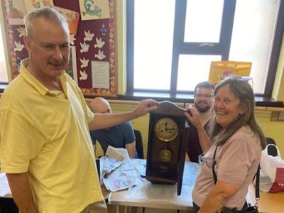 Two people standing next to a repaired clock