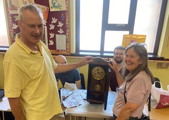 Two people standing next to a repaired clock